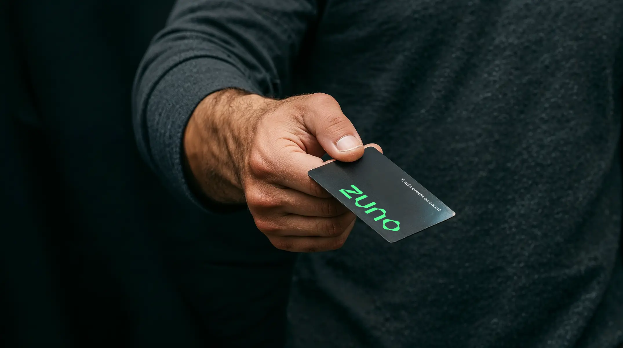 A hand holding a Zuno branded Trade credit card